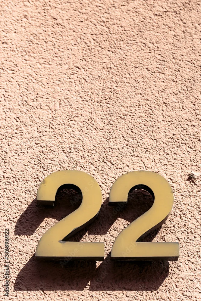 Number 22 Twenty Two Golden Metal Address Sign Fixed Onto Textured Peach Stone Wall Background